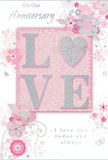 This anniversary card, ideal for marking a long-cherished romance in Lewisham, blends soft pastel pinks, pearly whites, and gentle silvery greys to create a quietly intimate mood. At the centre, the word LOVE is proudly displayed in raised, glitter-touched lettering, with the O transformed into a shimmering silver heart that feels both playful and deeply symbolic. The tactile surface of the lettering suggests that fingertips could follow its outline, much as one might trail a hand along the stems of a freshly arranged bouquet being carried home from Lewisham Shopping Centre. Surrounding the central word, delicate blossoms in blush and muted mauve appear to unfurl across the card's surface, painted in an almost watercolour softness. Their edges are defined with fine lines that hint at both artistry and care, like the practiced strokes of a florist sketching an anniversary arrangement before delivery. Tiny flourishes-petals, swirling tendrils, and a few discreet butterflies-add a sense of gentle motion, reminiscent of an English spring garden in quiet bloom, perhaps not far from Ladywell Fields. The card carries inscriptions such as On Our Anniversary and I love you today and always, written in a flowing, graceful script that feels personal and sincere without ever being overly ornate. Every element of the layout is balanced and considered, with plenty of soft space around the artwork, giving the card a refined, contemporary feel. It looks like a keepsake meant to be treasured in a memory box, a paper echo of the love, warmth, and shared journey it celebrates.